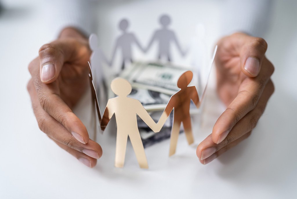 A pair of brown hands cradling a paper cutout of people holding hands around a pile of money, representing a community of people protecting and controlling their own funds.